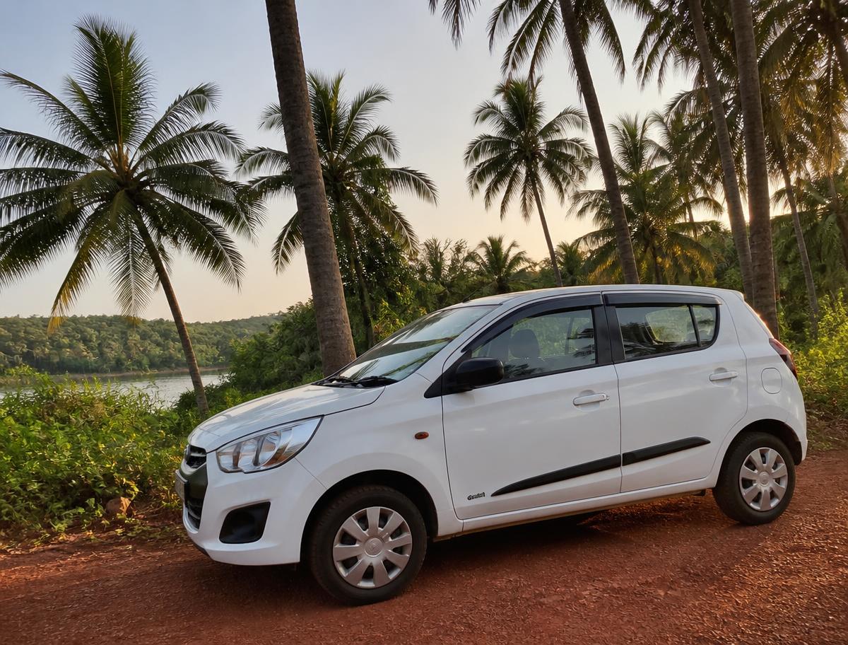 White rental car parked on a palm-lined red-earth road in North Goa
